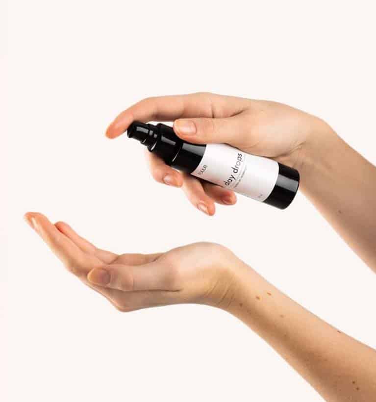Mooie handen houden PUUUR day drops vast. Een hand drukt op het pompje, terwijl de andere hand de vitamines en omega's opvangt.