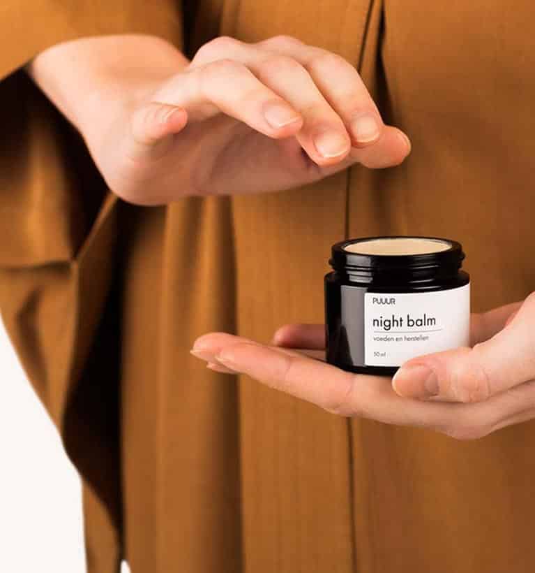 Vrouw die PUUUR night balm presenteert met geopend potje, waar de natuurlijke crème zichtbaar is voor effectieve huidverzorging.